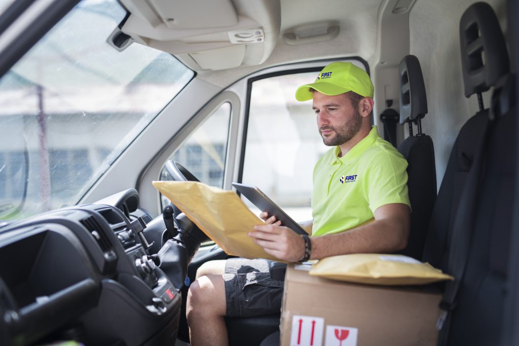 Man in delivery van holding parcel and checking digital tablet